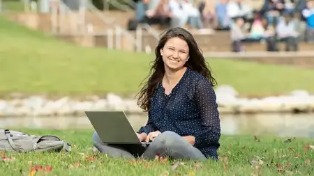 一个女人拿着笔记本电脑坐在湖边的草地上